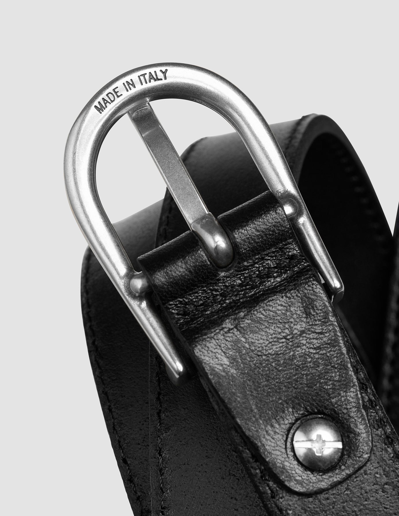 Nahaufnahme einer silberfarbenen Metallschnalle mit der Gravur „MADE IN ITALY“ an einem schmalen Damenledergürtel in Silber-Schwarz.